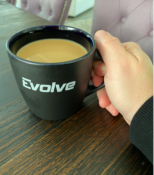 a hand holding a black coffee mug with a brown liquid in it